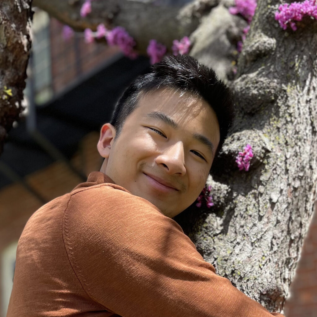 A close-up of a man's face in front of a tree with pink flowers